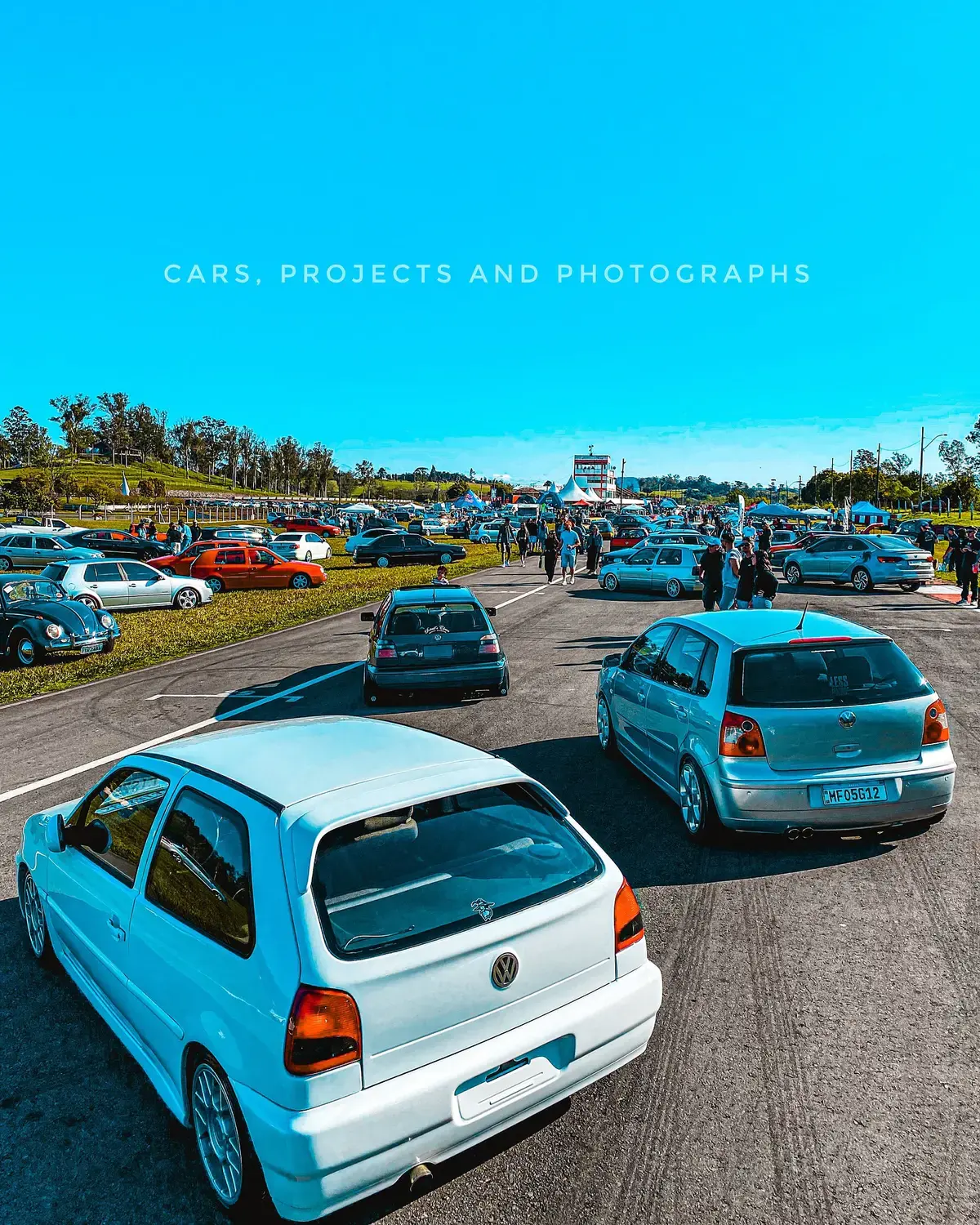 Volkswagens rebaixados em tons de azul alinhados sobre o gramado de um encontro.